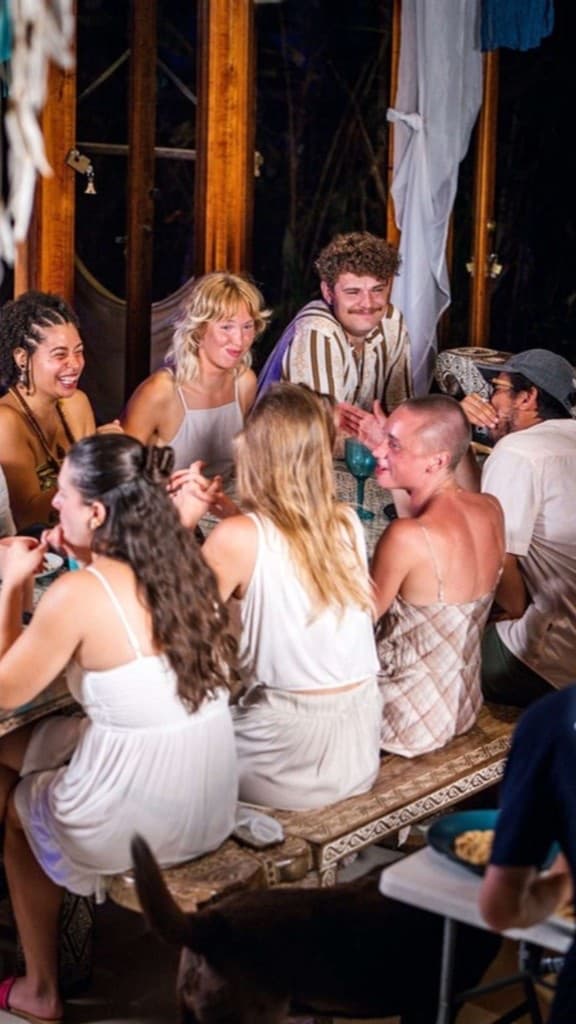 Guests laughing together around a wooden table during an evening gathering at the retreat