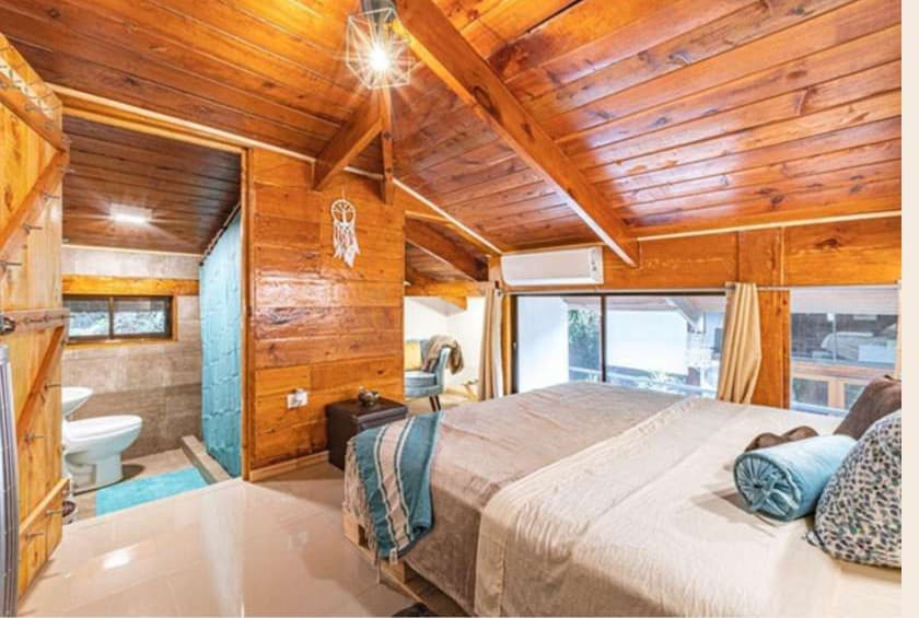 Warm wood-paneled bedroom with white linens and an en-suite bathroom at Villa Wanderlust