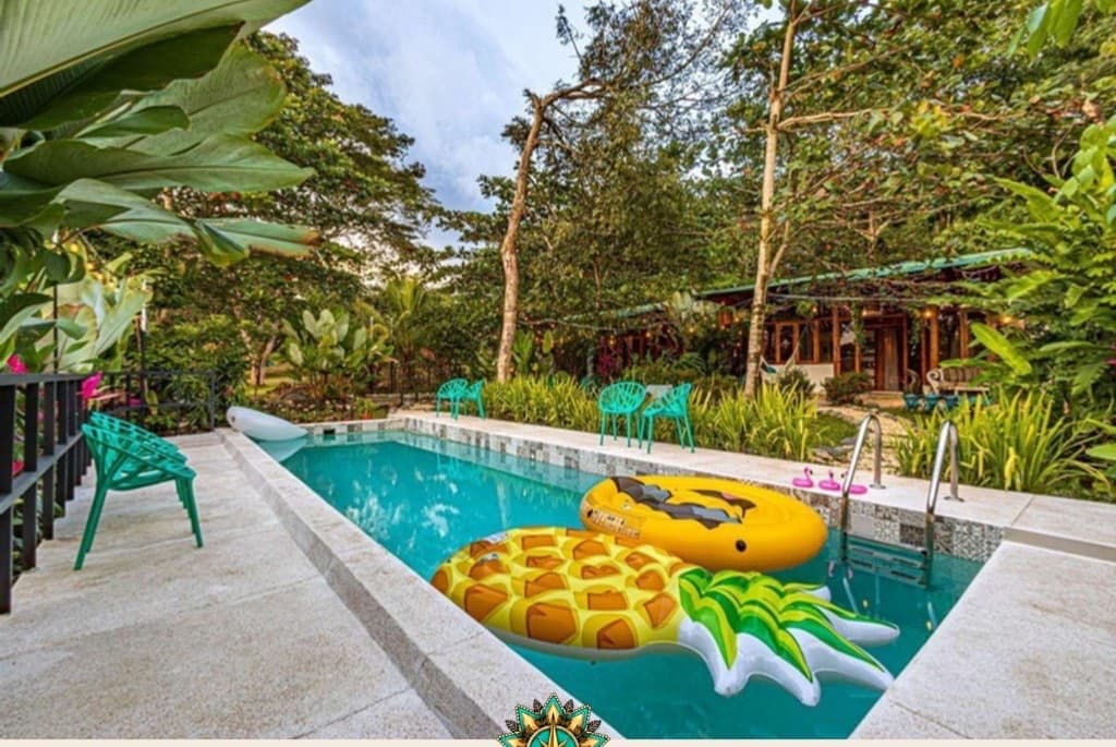 Turquoise daytime pool with tropical foliage and teal seating at Villa Wanderlust