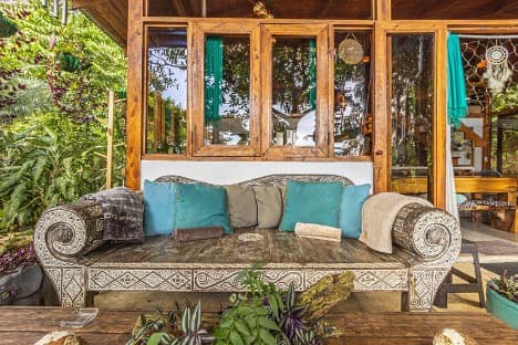 Carved wooden daybed with teal cushions in a lush outdoor lounge area